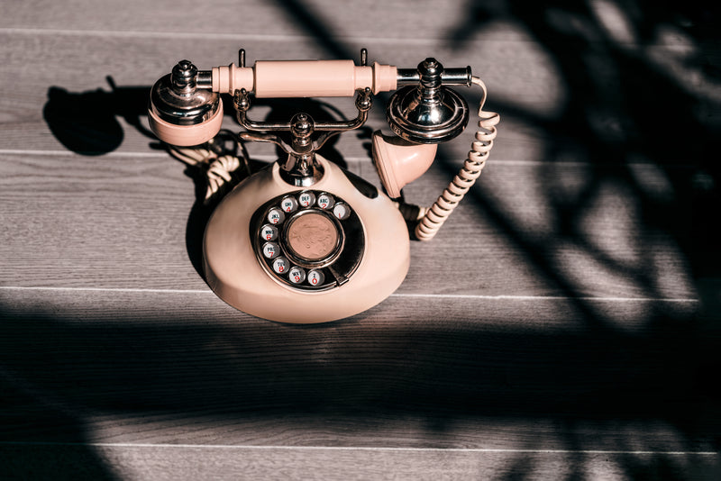 An old-fashioned pink rotary phone sitting on a wooden table with a dramatic shadow.